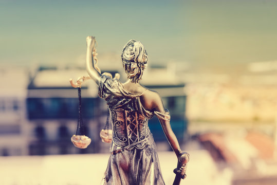 Back view of Lady Justice, statuette of the Themis goddess. Law concept. City buildings outdoor background