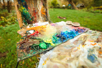 Professional artist's sketchbook with multicolored palette of blended oil paints and paintbrushes outdoors.