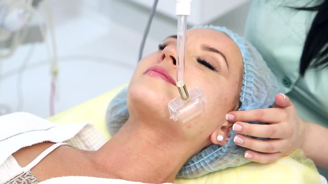 Receiving electric darsonval facial massage procedure.