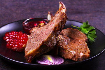 Grilled rack of lamb with pomegranate sauce in black plate on dark textural background