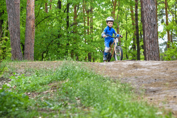 Obraz premium Happy funny little kid boy in colorful raincoat riding his first bike on cold day in forest. Active leisure for children outdoors. carefree childhood concept