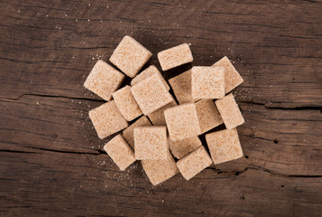 Brown cane sugar cubes on wooden background. top view