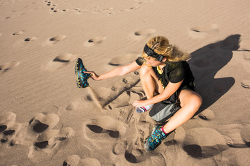 Fototapeta na wymiar Young woman sitting pouring out sand from shoes sneakers in dunes