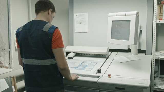 Poligraphy industry - worker checks colours and use touch screen monitor for printed process, rear view