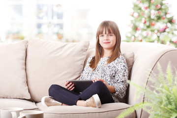 Cute girl at christmas tree. Portrait of cute little girl using digital tablet while sitting at couch at christmas tree.