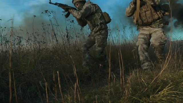 Ukrainian soldier aims and walk on the field through the smoke.