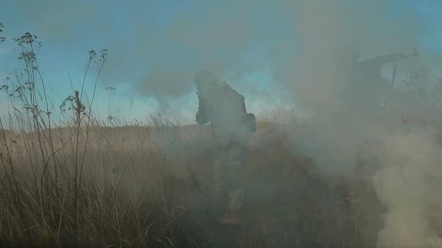 Ukrainian soldier aims, stand and walk on the field through the smoke.