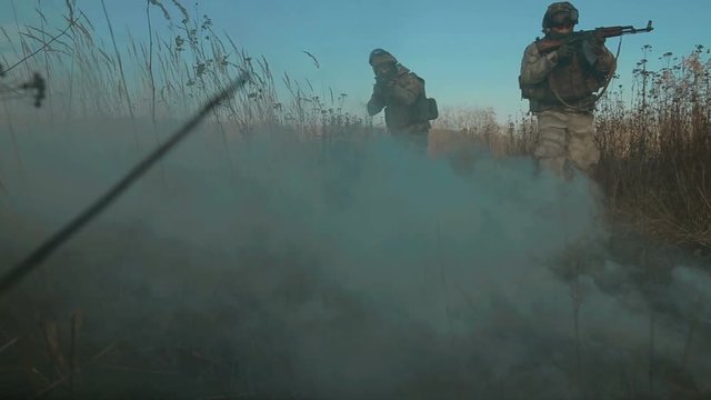 Ukrainian soldier aims and walk on the field through the smoke.