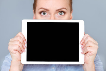Your text is here. Beautiful woman hiding her face behind digital tablet with copy space while standing against grey background