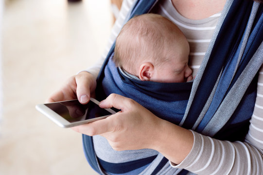 Unrecognizable mother with her son in sling, holding smartphone