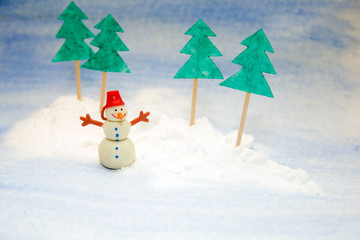 little snowman in the snow among paper trees