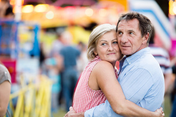 Senior couple at the fun fair, hugging. Sunny summer.