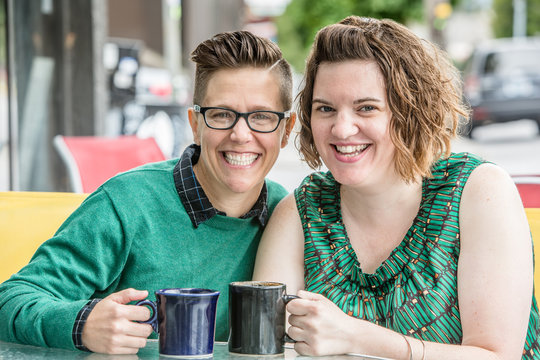 Happy Lesbian Couple Sitting At Table Outside