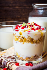 Healthy breakfast with yogurt, muesli and pomegranate berries in glass on wooden background