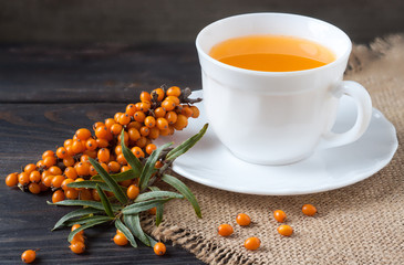 Obraz na płótnie Canvas Tea of sea-buckthorn berries with a sprig on sackcloth and wooden background