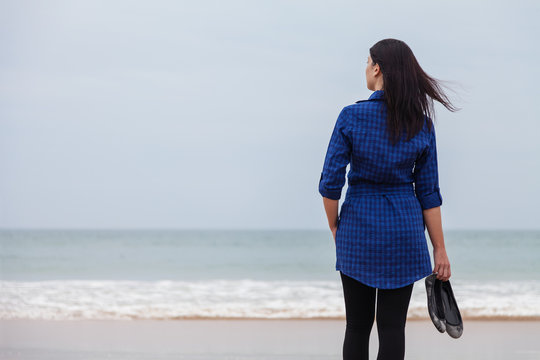 Lonely and depressed woman standing in front of the sea in a deserted beach on an Autumn day.