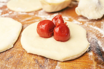 Preparing homemade ukrainian dumplings or varenyky, cutting the round pieces of dough with cherry