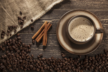 Coffee background. Ground coffee with foam with coffee beans on a wooden dark table with cinnamon sticks.