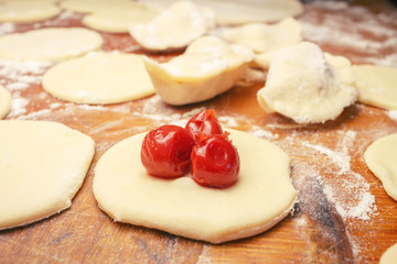 Preparing homemade ukrainian dumplings or varenyky, cutting the round pieces of dough with cherry