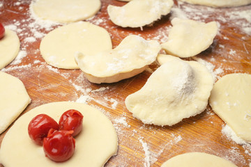 Preparing homemade ukrainian dumplings or varenyky, cutting the round pieces of dough with cherry
