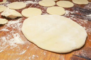 Preparing homemade ukrainian dumplings or varenyky, cutting the round pieces of dough with cherry