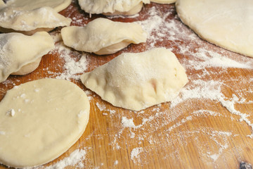 Preparing homemade ukrainian dumplings or varenyky, cutting the round pieces of dough with cherry