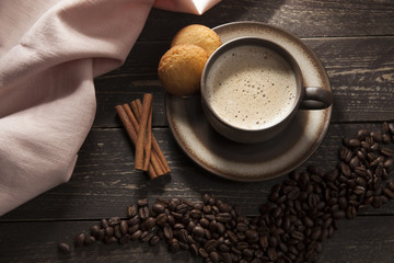 Fototapety  Tło kawy. Kawa mielona z pianką z ziarnami kawy na drewnianym ciemnym stole z laskami cynamonu i maślanymi kruche ciasteczkami.
