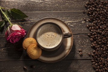Coffee background. Ground coffee with foam with coffee beans on a wooden dark table with butter shortbreads and a rose flower.