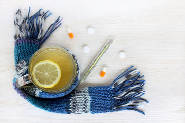 plentiful drink while colds/ Tea with lemon in a transparent cup wrapped in scarf next to the pills...
