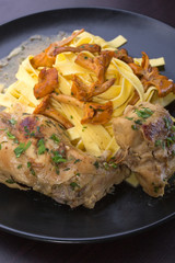 Braised rabbit with Italian pasta tagliatelle and Gérin chanterelles mushrooms on a black plate. homemade food