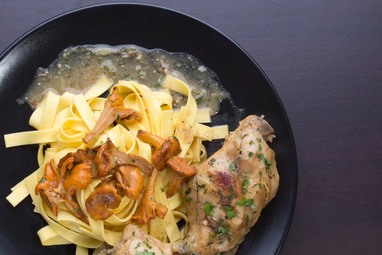 Braised rabbit with Italian pasta tagliatelle and Gérin chanterelles mushrooms on a black plate. homemade food