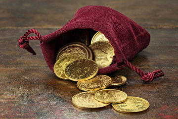 various European circulation gold coins from the 19th/20th century in a velvet purse on rustic wooden background