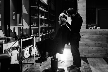 Obraz premium The Barber man in the process of cutting a customer in the barbershop, a black-and-white photo