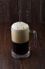 Dark beer mug with foam and drops wood background