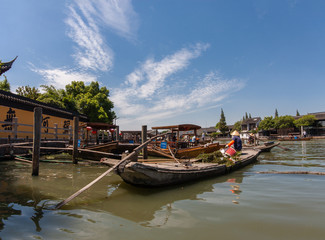 Fototapeta premium Boatman transports underwater grass by boat made of concrete on canal of ancient water town in Zhujiajiao, China