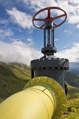 Yellow gas pipe line valves with mountains background and blue sky with clouds