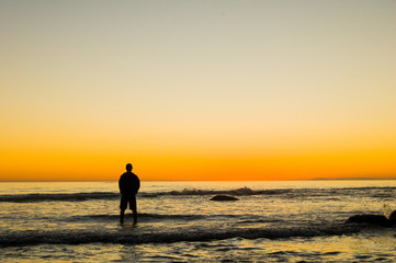Silhouette of a man standing on the beach in the surf watching the beautiful sunset