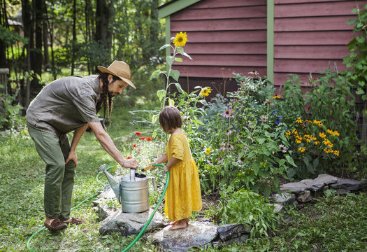 Father looking at girl filling water with hose in watering can
