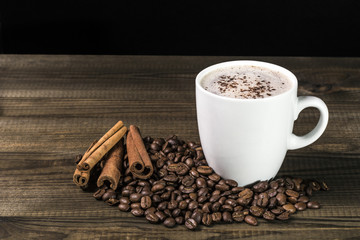 cup of coffee with coffee beans and cinnamon on wooden table. Image with copy space