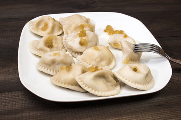 Traditional polish dumplings, "pierogi ruskie" on white plate on wooden table.