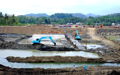 Naklejka premium Blue Excavator working in construction site and few worker appear walking in the site