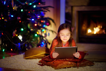 Adorable little girl using a tablet pc by a fireplace on Christmas evening