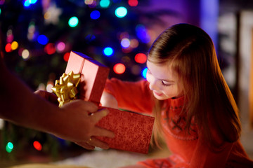 Happy little girl getting a Christmas gift from her parent