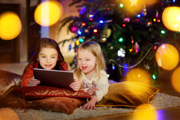 Fototapeta na wymiar Two cute little sisters using a tablet pc by a fireplace on Christmas evening