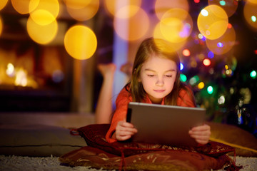 Adorable little girl using a tablet pc by a fireplace on Christmas evening