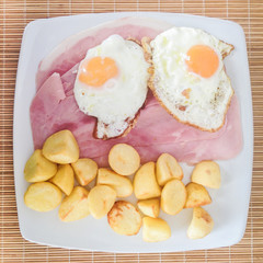 Ham with fried eggs and potatoes on a white plate