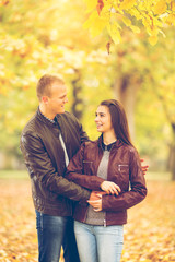 Fototapeta premium Young couple are enjoying therig time together in a park on a beautiful Autumn day. They look at each other and smile.