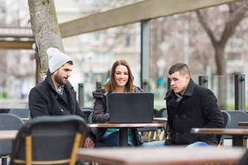 Three happy friends with laptop outside in a coffee shop