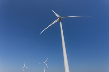 Wind generators from below, against a blue sky.