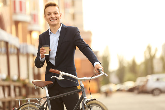 Coffee-to-go concept. Young man with bicycle and cup of coffee on street
